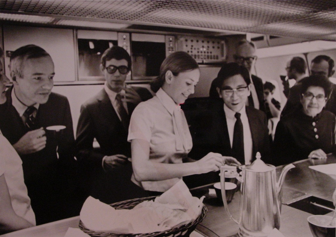 1970s A flight attendant pours coffee in the main galley of a Pan Am 747.  These passengers are members of the Press on an publicity flight.